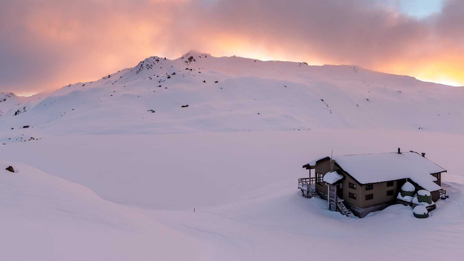 Mountain hut standing in deep snow below a ridge