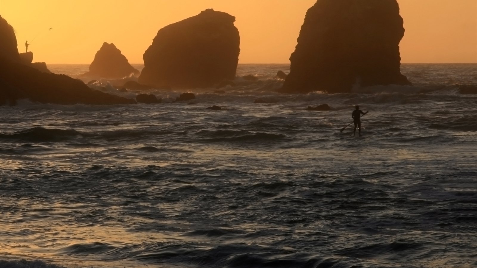 Lone paddleboarder crossing golden water at sunset