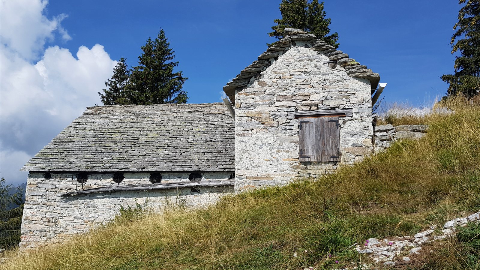 Stone mountain hut with a slate roof on a grassy slope
