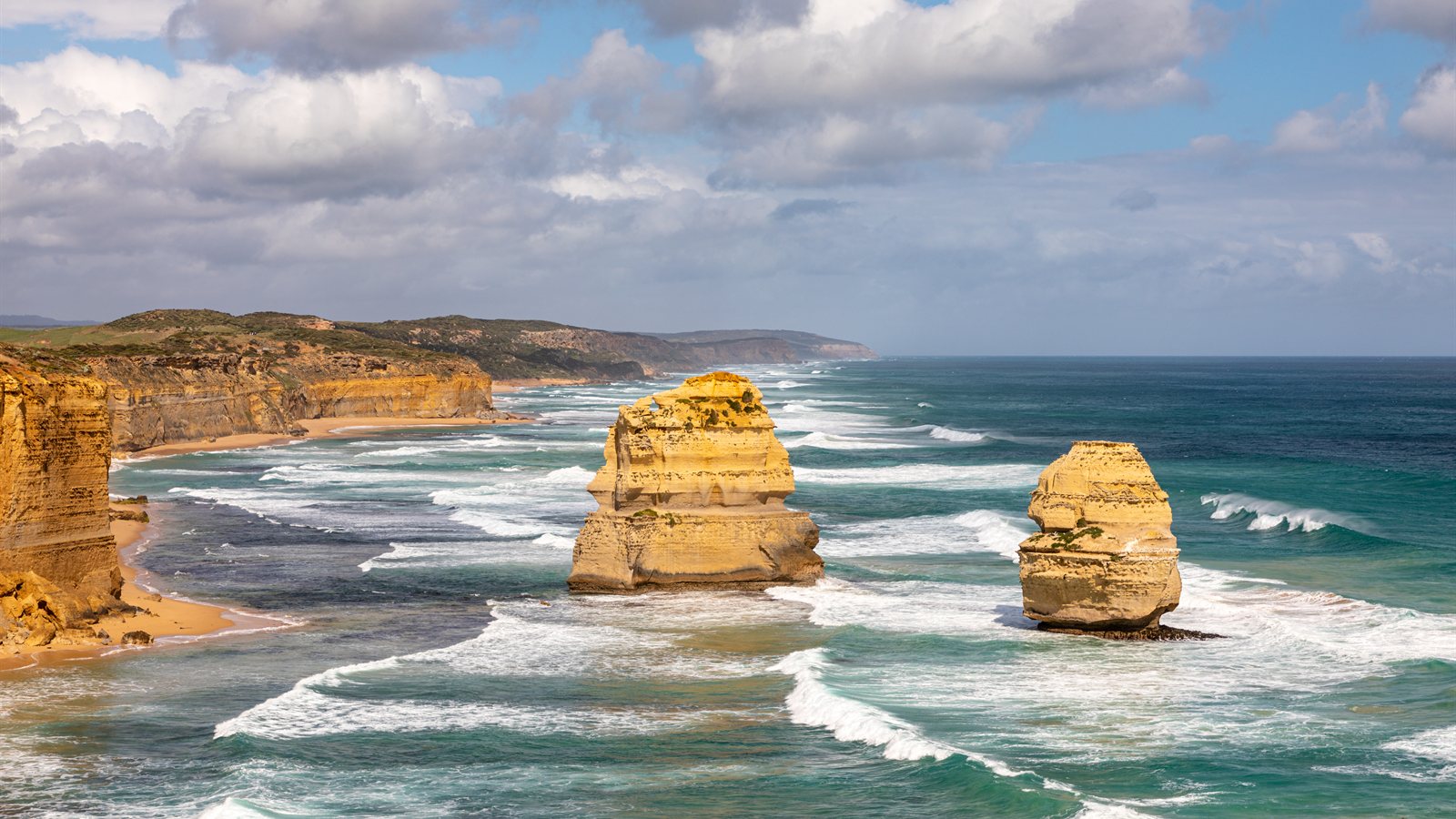 Rock stacks standing offshore in the surf under a bright sky