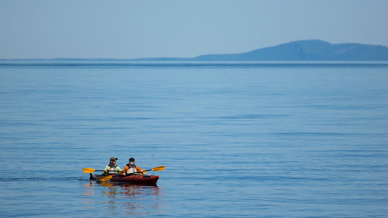 Tandem kayak crossing wide open water in bright morning light