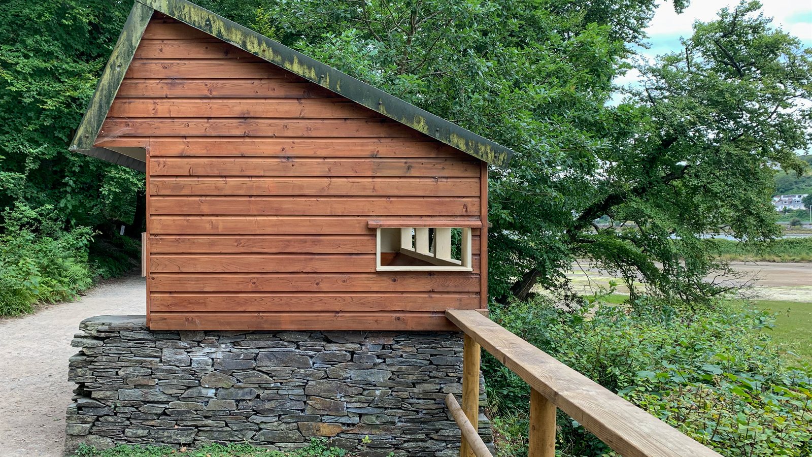 Timber birdwatching hide on a stone base beside a path