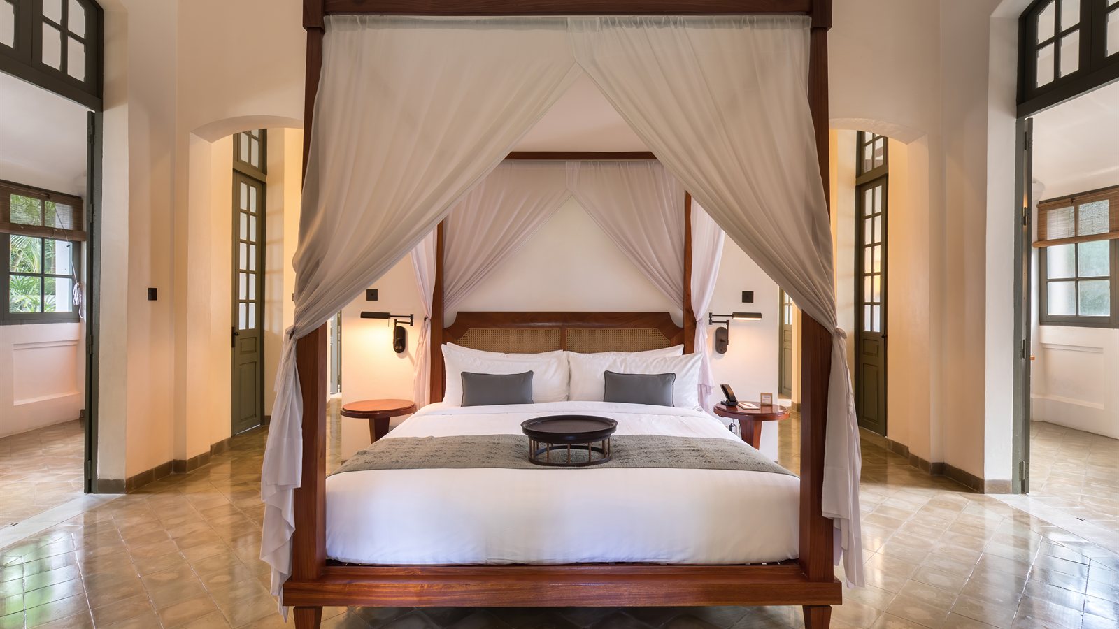 Four-poster bed in a bright room with tall shuttered doors