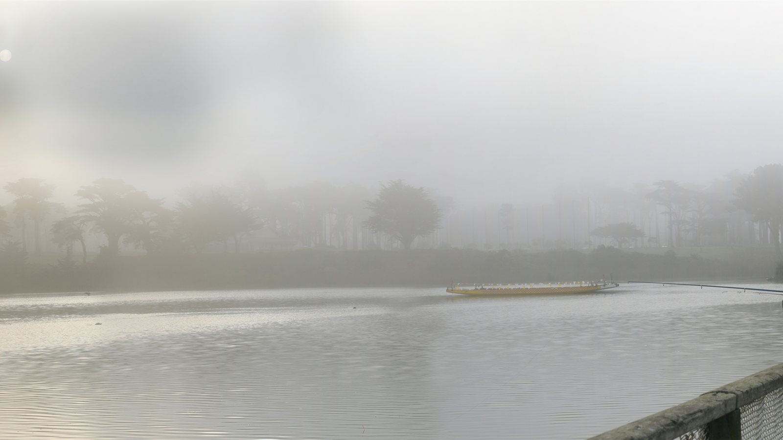 Foggy lakeside promenade with a lone figure at the rail