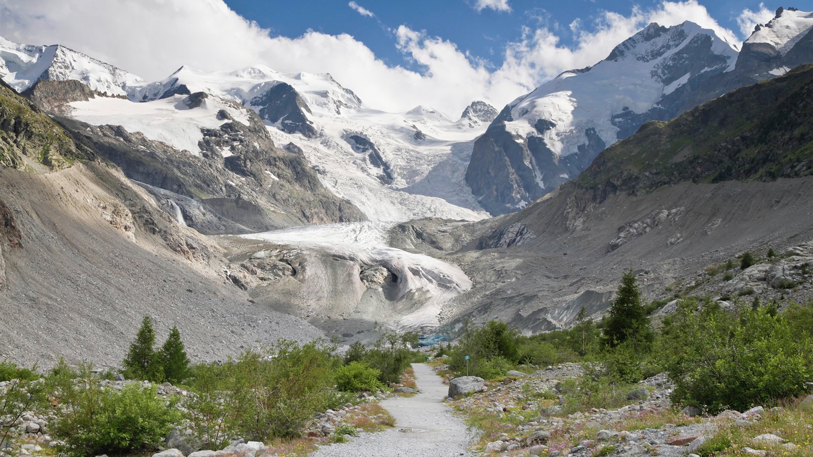 Gravel trail leading towards snow-covered peaks in a wide valley