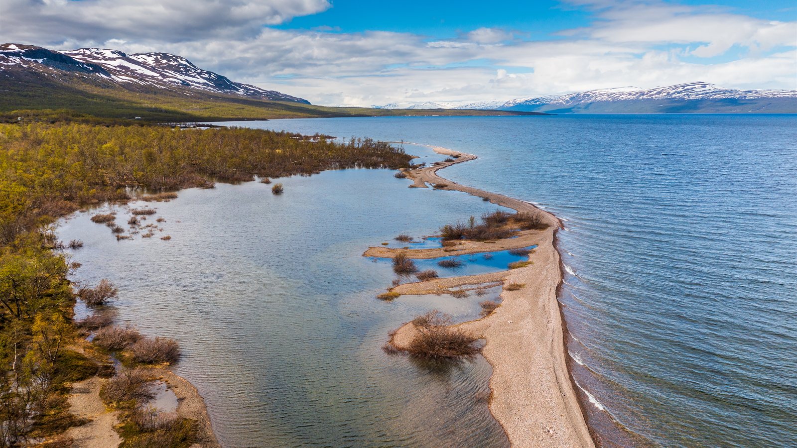 Narrow gravel spit reaching into a bright northern lake