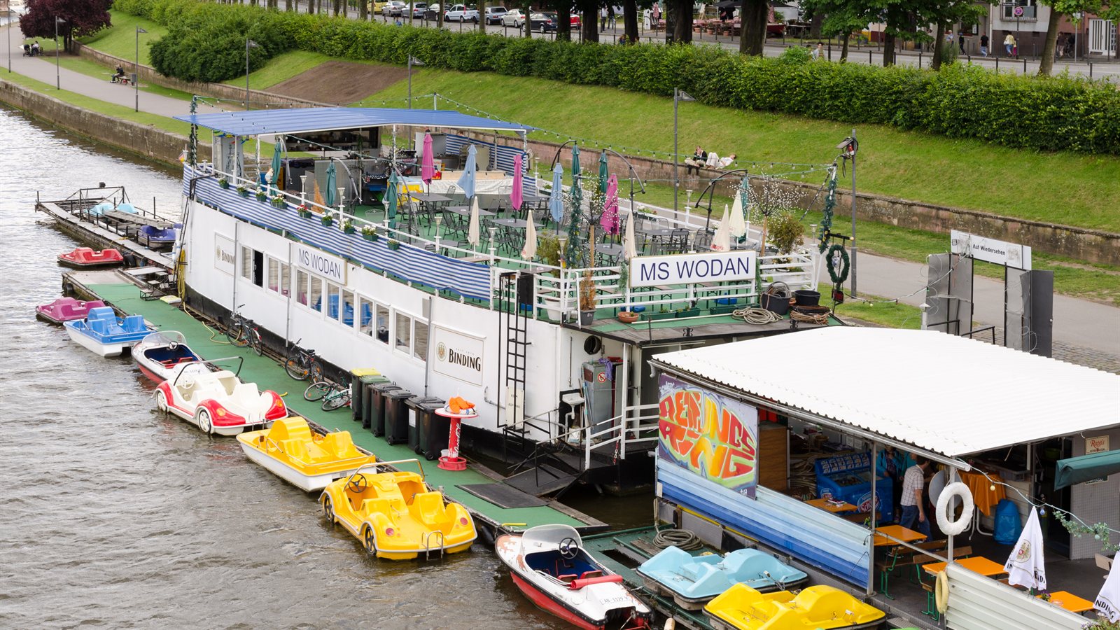 Moored restaurant vessel with pedal boats along a city embankment