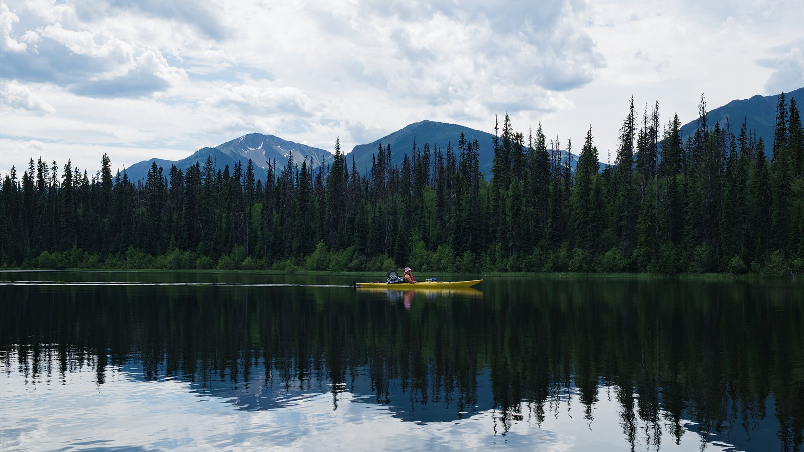 Paddler crossing a still mountain lake